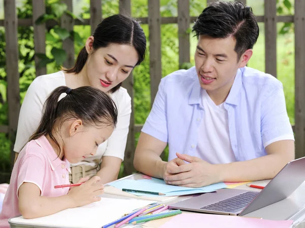 Young parents help their children with their homework outdoors