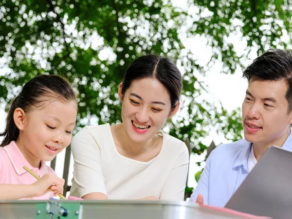 Jovens pais ajudam seus filhos com seus trabalhos de casa ao ar livre — Fotografia de Stock