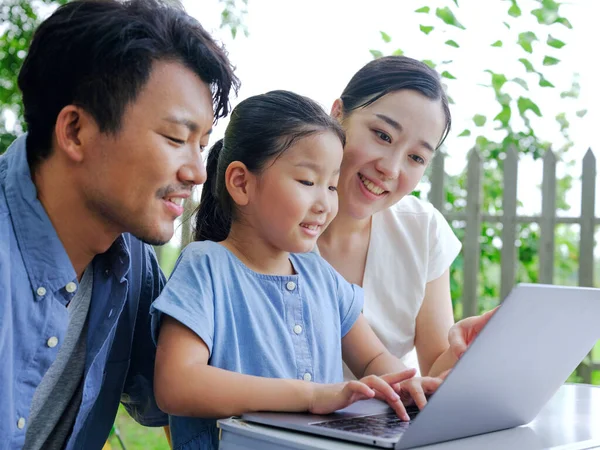 Lycklig familj av tre använda dator för att surfa på Internet utomhus — Stockfoto