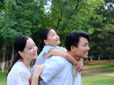 Üç kişilik mutlu bir aile parkta oynuyor.