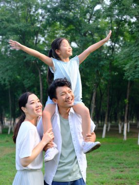 Üç kişilik mutlu bir aile parkta oynuyor.