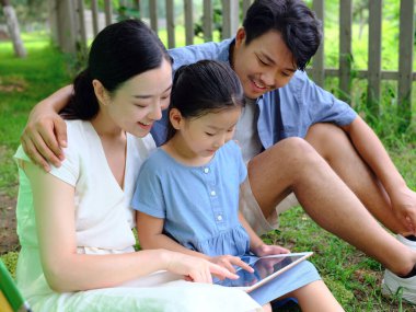 Üç kişilik mutlu bir aile dışarıda tablet bilgisayar kullanıyor.