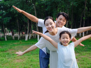 Üç kişilik mutlu bir aile parkta oynuyor.
