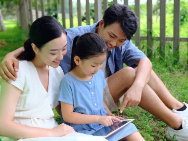 Üç kişilik mutlu bir aile dışarıda tablet bilgisayar kullanıyor.