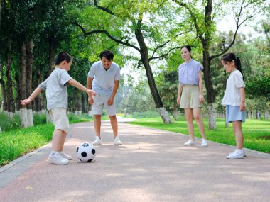 Parkta futbol oynayan dört kişilik mutlu bir aile.
