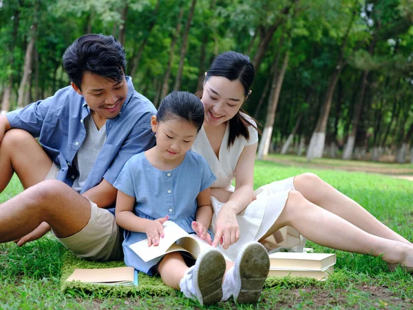 A happy family of three is reading outdoors