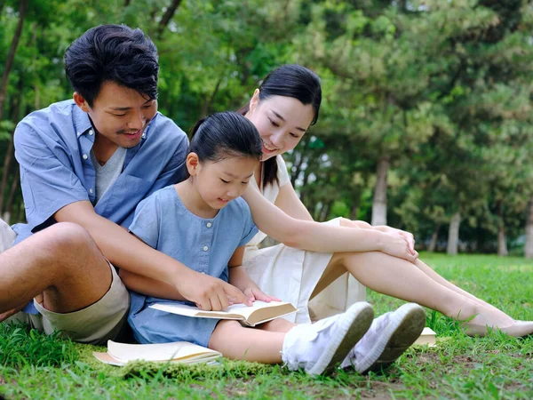En lycklig familj på tre personer läser utomhus — Stockfoto
