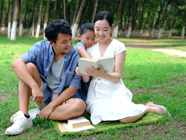 Uma família feliz de três está lendo ao ar livre — Fotografia de Stock