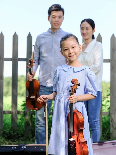 Happy family of three playing violin in the park