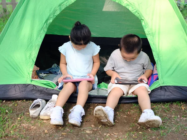 Çadırda tabletlerle oynayan iki çocuk.