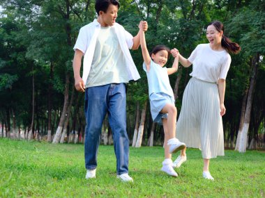 Üç kişilik mutlu bir aile parkta oynuyor.