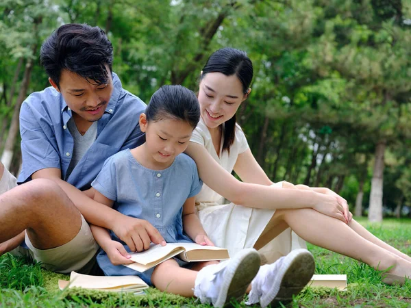 Uma família feliz de três está lendo ao ar livre — Fotografia de Stock