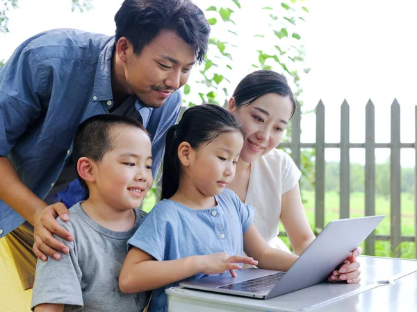 Happy family of four use computer to surf the Internet outdoors — Stock Photo, Image