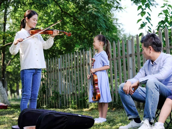 Família feliz de três tocando violino no parque — Fotografia de Stock