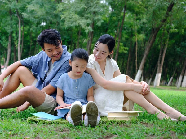 Egy boldog háromtagú család olvas a szabadban. — Stock Fotó