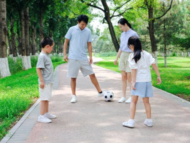 Parkta futbol oynayan dört kişilik mutlu bir aile.
