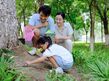 Üç kişilik mutlu bir aile dışarıda böcek yakalar.