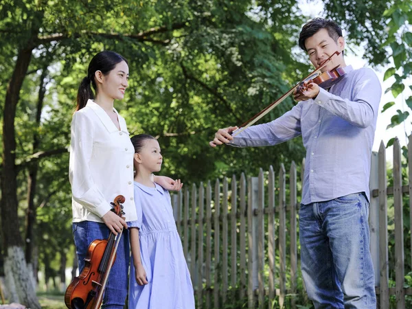 Família feliz de três tocando violino no parque — Fotografia de Stock