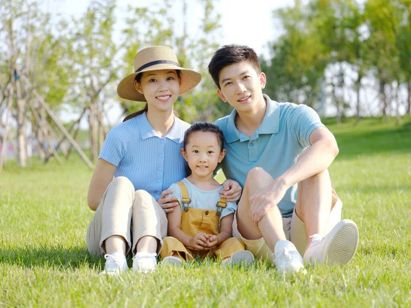 Üç kişilik mutlu bir aile çimlerin üzerinde oturuyor. — Stok fotoğraf