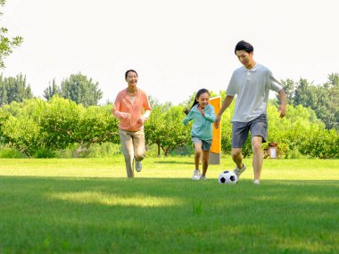 Parkta futbol oynayan mutlu üç kişilik bir aile.