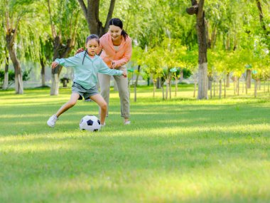 Mutlu anne ve kız parkta futbol oynuyorlar.