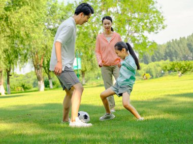 Parkta futbol oynayan mutlu üç kişilik bir aile.