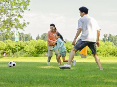 Parkta futbol oynayan mutlu üç kişilik bir aile.