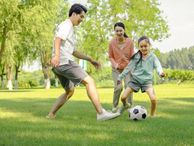Parkta futbol oynayan mutlu üç kişilik bir aile.