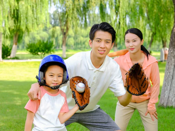 Boldog háromtagú család baseballozik a parkban. — Stock Fotó