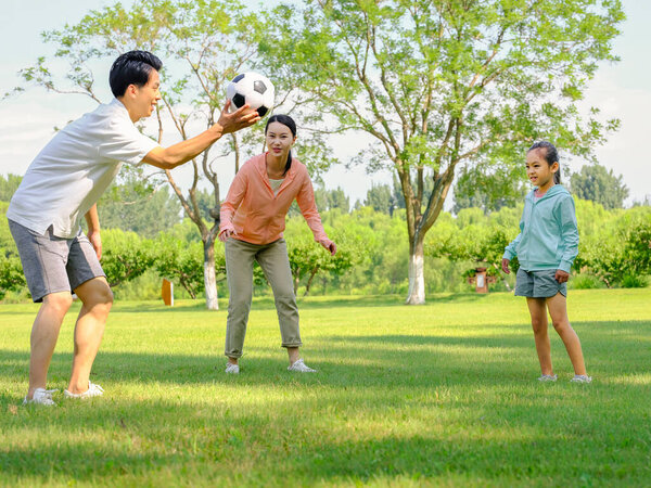 Счастливая семья из трех человек играет в футбол в парке
