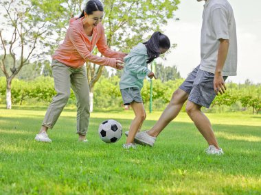 Parkta futbol oynayan mutlu üç kişilik bir aile.