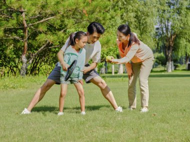 Parkta tenis oynayan üç kişilik mutlu bir aile.