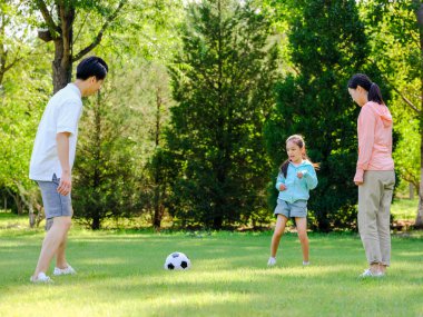 Parkta futbol oynayan mutlu üç kişilik bir aile.