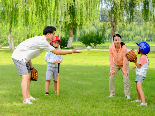 Happy family of four playing baseball in the park — Stock Photo, Image