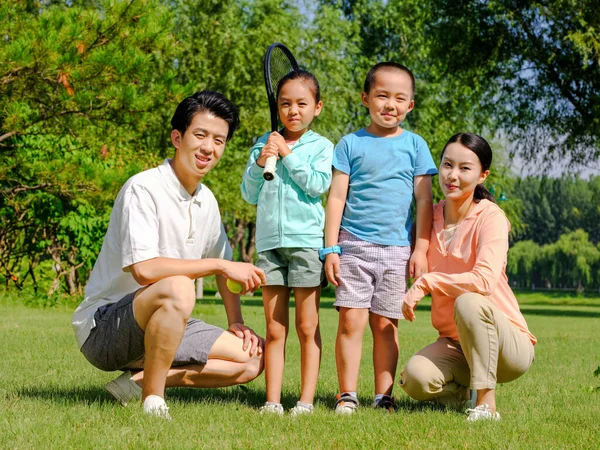 Família feliz de quatro jogando tênis no parque — Fotografia de Stock