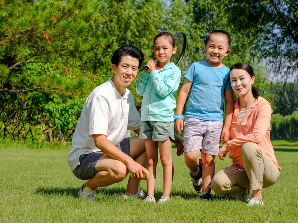 Família feliz de quatro jogando tênis no parque — Fotografia de Stock