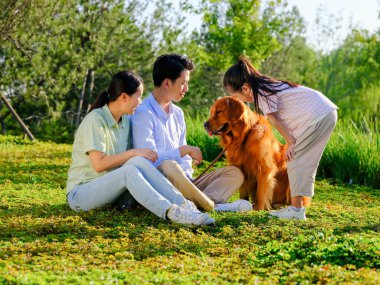 Üç kişilik mutlu bir aile ve parkta oynayan evcil bir köpek.