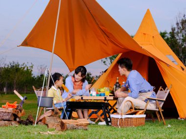 Üç kişilik mutlu bir aile parkta barbekü yapıyor.