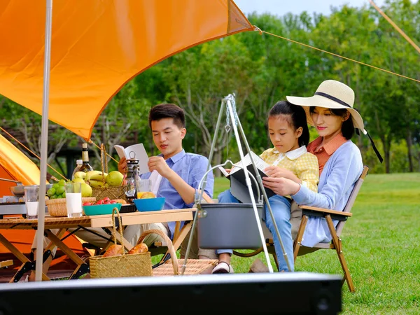 Счастливая семья из трех человек читает снаружи — стоковое фото