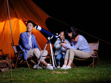 A happy family of three using telescopes outdoors clipart