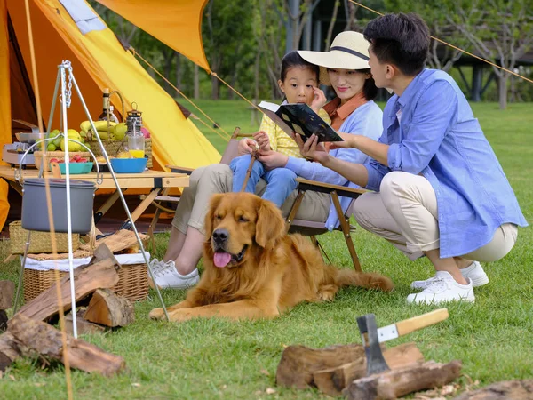 Heureuse famille de trois et chien de compagnie lisant à l'extérieur — Photo