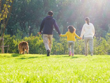 Üç kişilik mutlu bir aile ve parkta yürüyen evcil bir köpek.