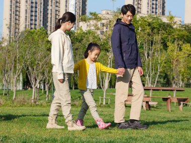 Üç kişilik mutlu bir aile parkta yürüyor.