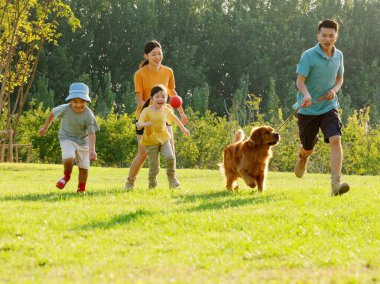 Dört kişilik mutlu bir aile ve parkta oynayan evcil bir köpek