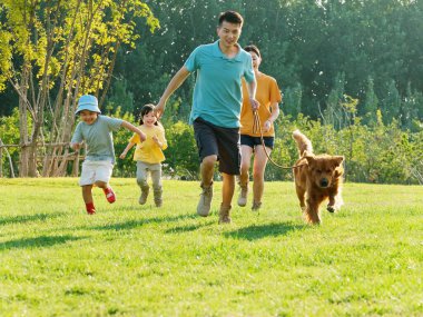 Dört kişilik mutlu bir aile ve parkta oynayan evcil bir köpek