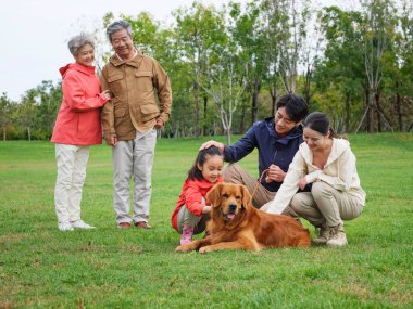 Mutlu beş kişilik bir aile ve parkta oynayan bir köpek.