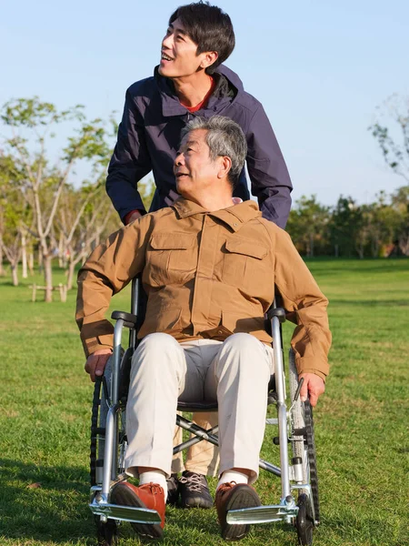 O jovem empurrou o velho na cadeira de rodas para um passeio — Fotografia de Stock