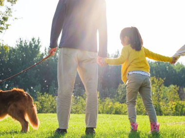 Üç kişilik mutlu bir aile ve parkta yürüyen evcil bir köpek.