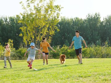 Dört kişilik mutlu bir aile ve parkta oynayan evcil bir köpek