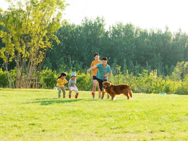 Happy family of four and pet dog playing in the park clipart